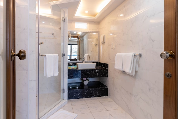 A modern bathroom with a glass shower enclosure, a black marble sink, and white marble walls. - Palma Beach Resort and Spa (Umm al Quwain)