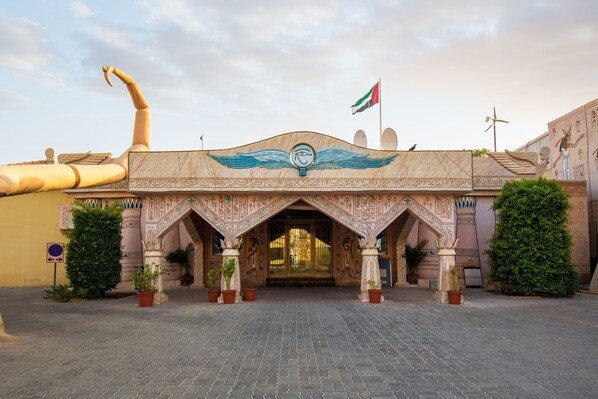 An entrance with intricate Egyptian-style carvings, a flag, and potted plants. - Palma Beach Resort and Spa (Umm al Quwain)
