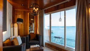 Una habitación acogedora con techo de madera, un ventanal con vista al mar, un sofá, una mesa de centro y una lámpara colgante.