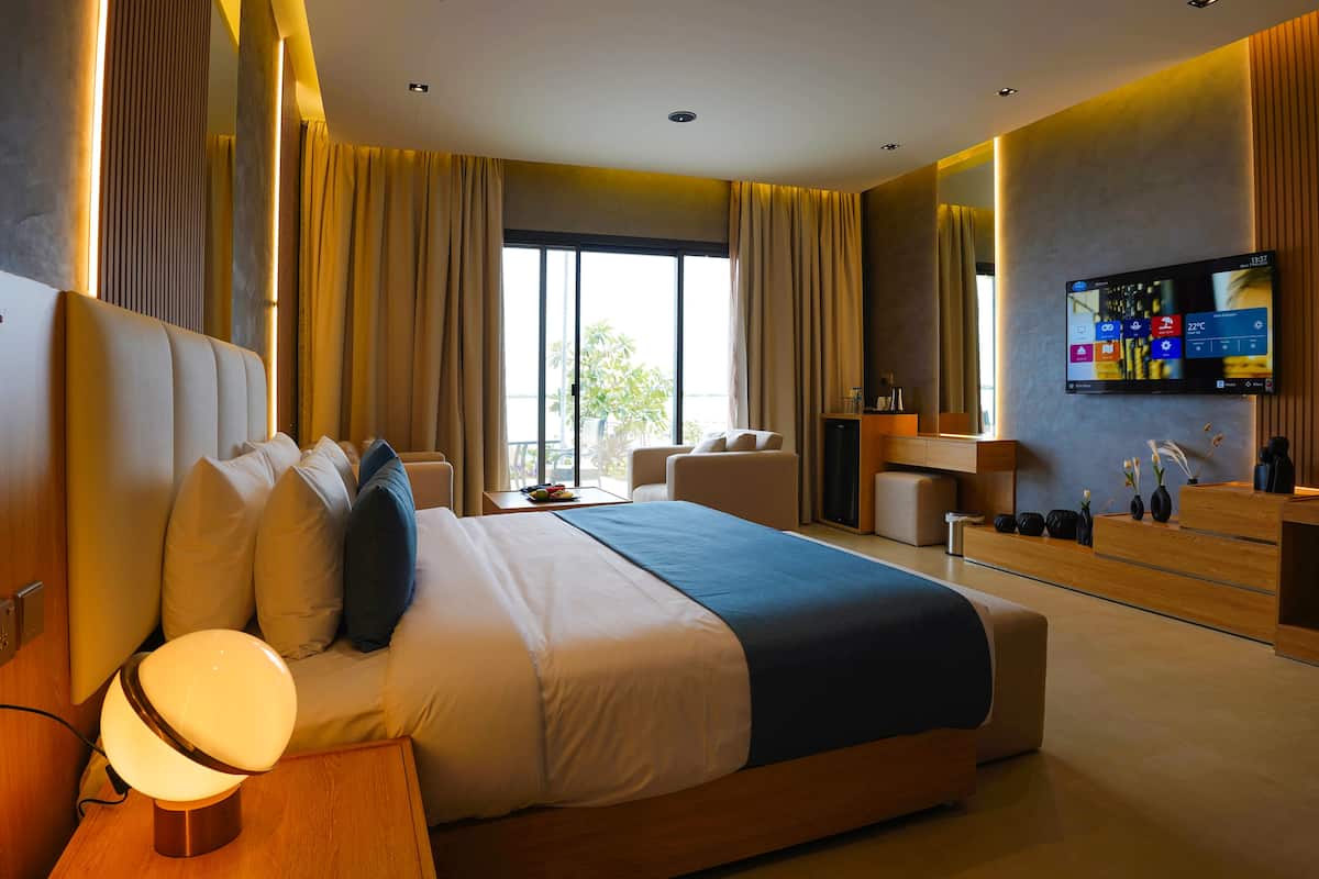 A modern hotel room with a large bed, a desk, a chair, a TV, and a view of the outdoors.