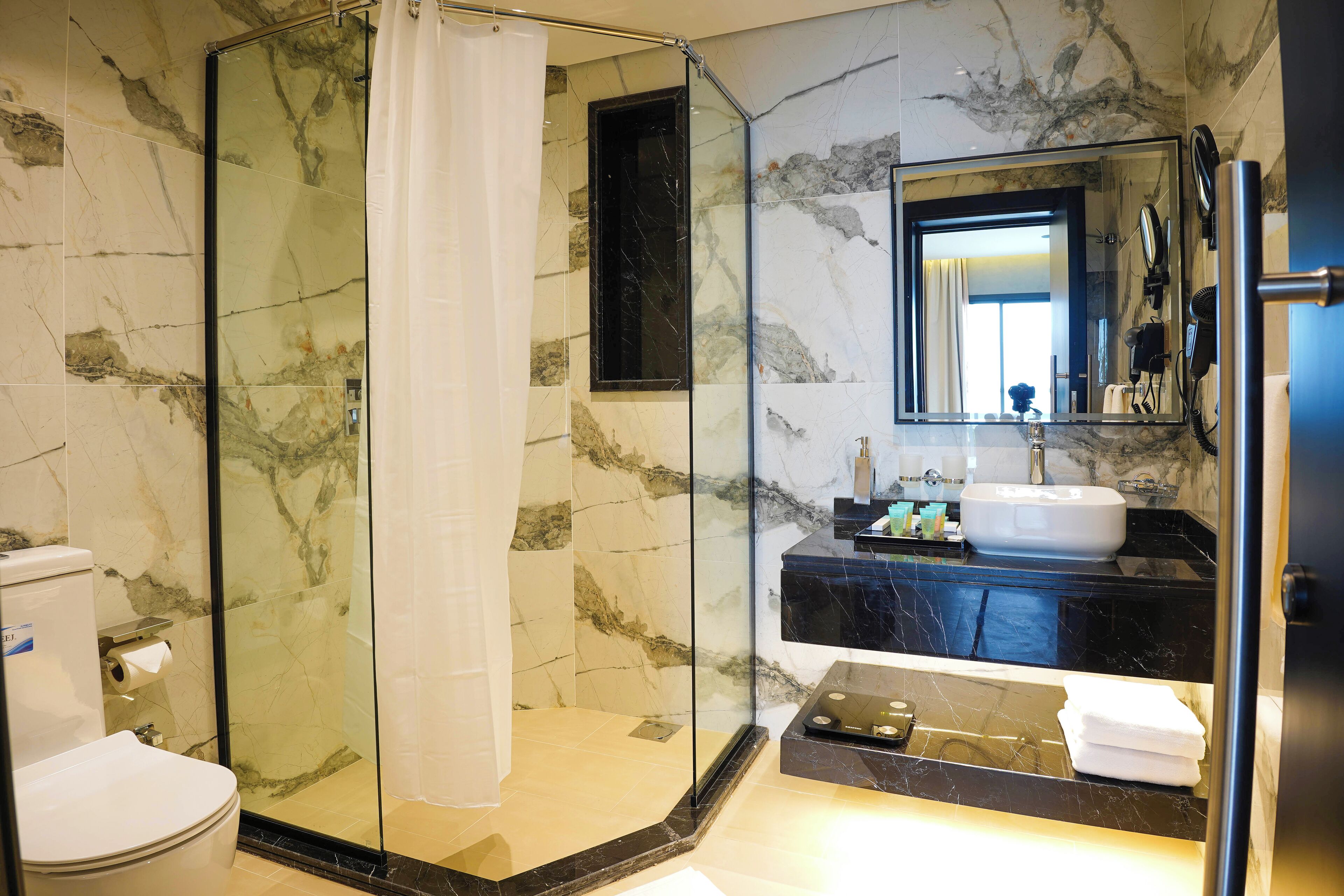 Un baño moderno con cabina de ducha acristalada, pared con azulejos de mármol, lavabo con encimera negra y un espejo grande.