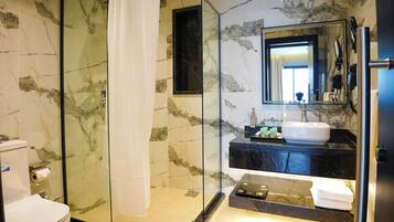 Un baño moderno con cabina de ducha acristalada, pared con azulejos de mármol, lavabo con encimera negra y un espejo grande.