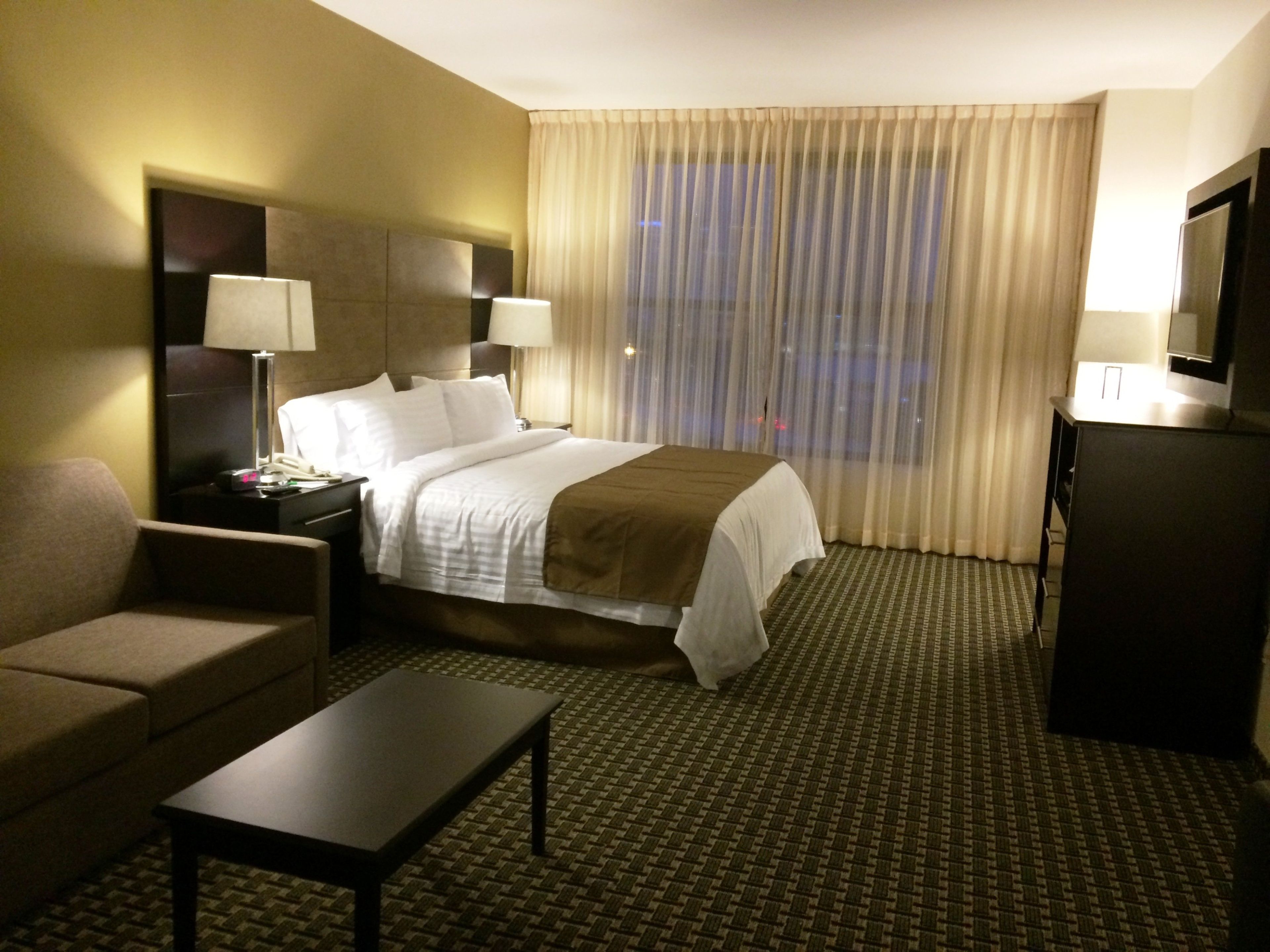 Een hotelkamer met een bed, een bureau, een stoel, een televisie en een raam met gordijnen.