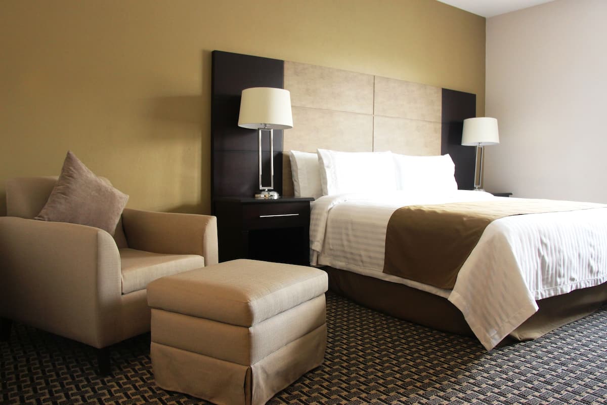 A hotel room with a bed, two bedside tables, a chair, and an ottoman.