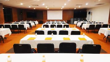 A conference room with multiple tables, chairs, and a large screen at the front.