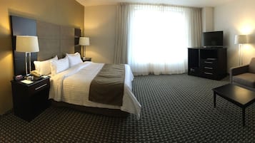 A hotel room with a bed, a desk, a chair, a sofa, a TV, and a mirror.