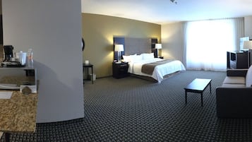 A hotel room with a kitchenette, a bed, a desk, and a bathroom.
