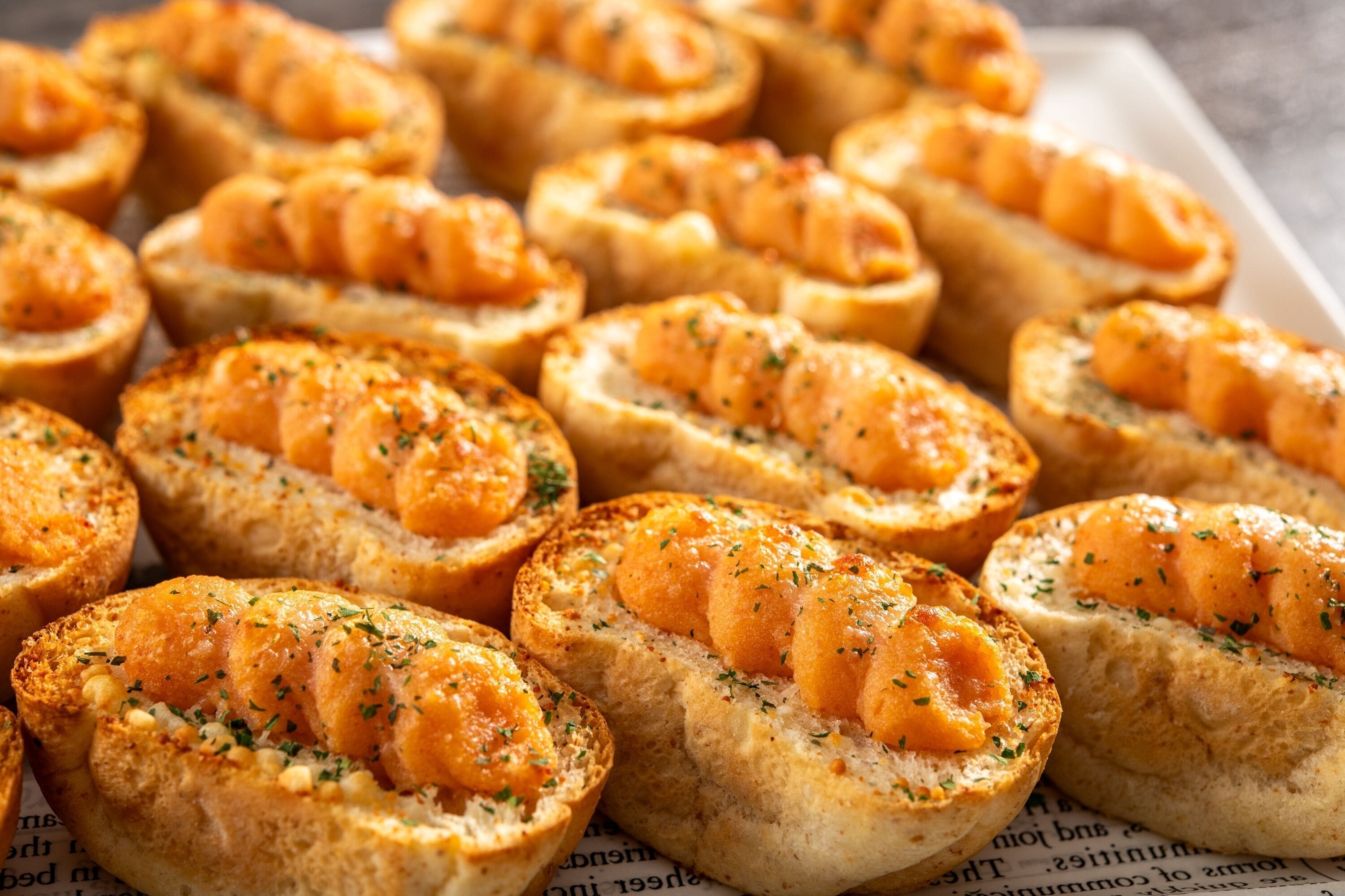 A tray of bread rolls filled with a golden-brown spread, garnished with herbs.