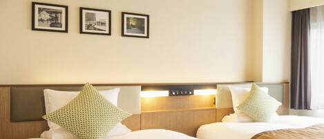 A hotel room with two beds, a wooden headboard, a nightstand with a lamp, and three framed pictures on the wall.