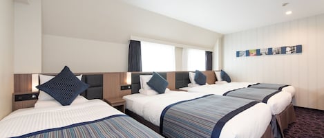 Habitación de hotel con tres camas, cada una con colcha a rayas y almohadas a juego. La habitación tiene un ventanal grande con cortinas, una obra de arte colgada en la pared y piso alfombrado.