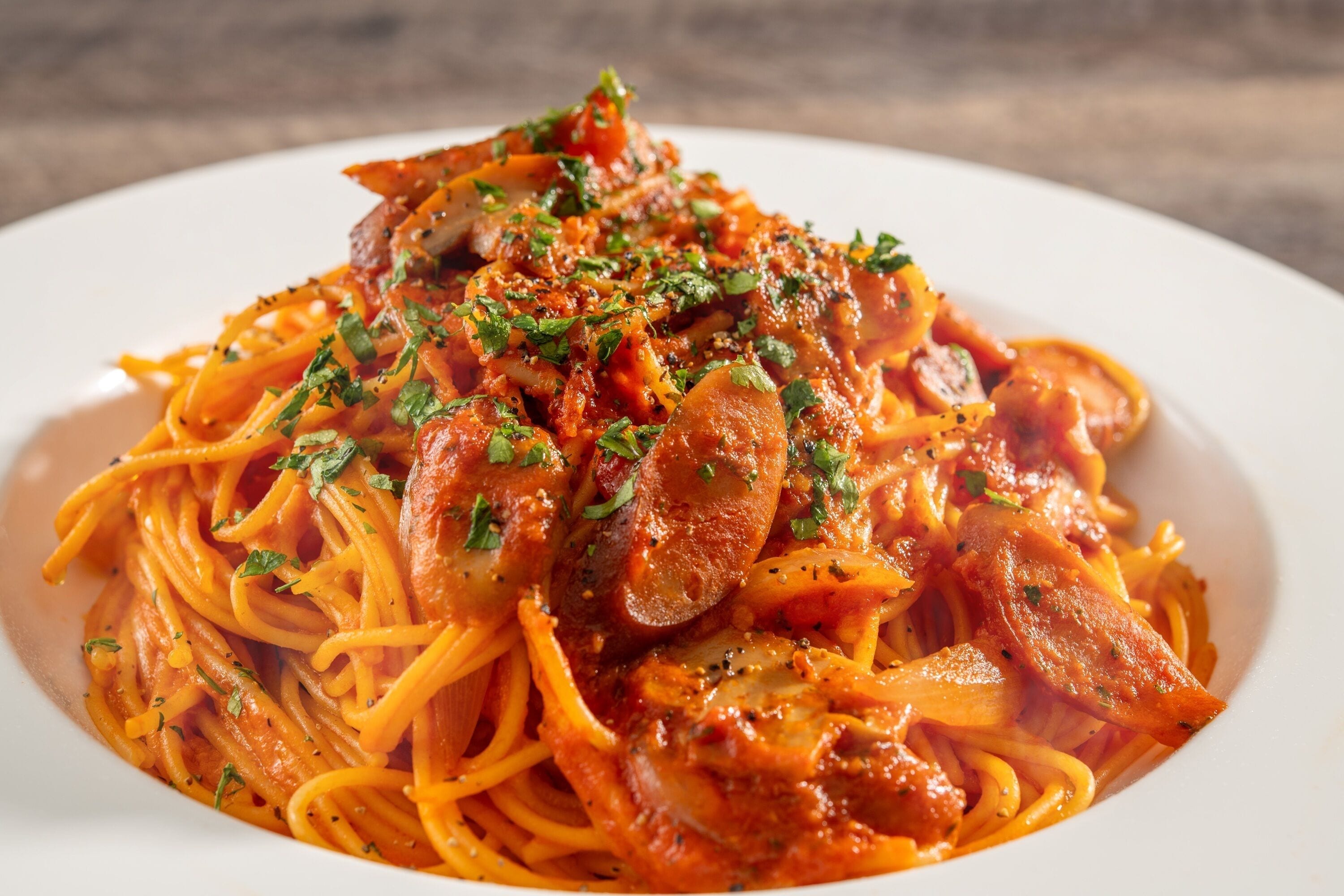 A plate of spaghetti with sausage and tomato sauce, garnished with herbs.