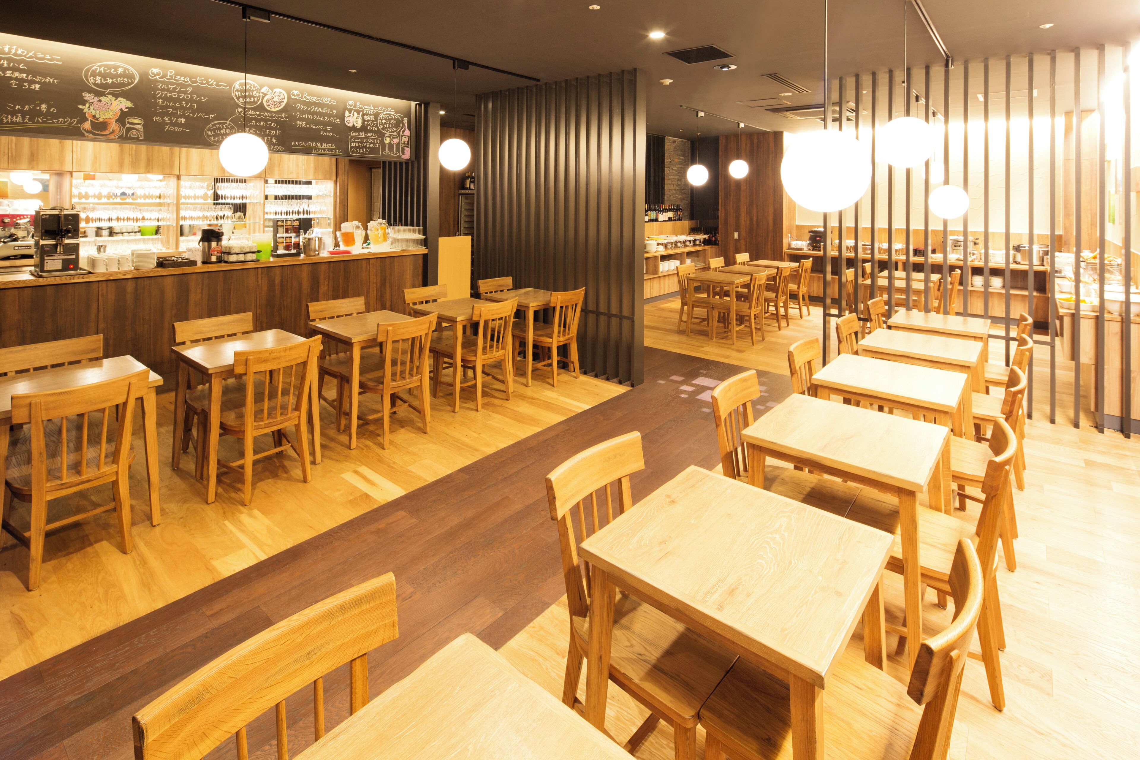 A restaurant with wooden tables and chairs, a bar area, and hanging lights.