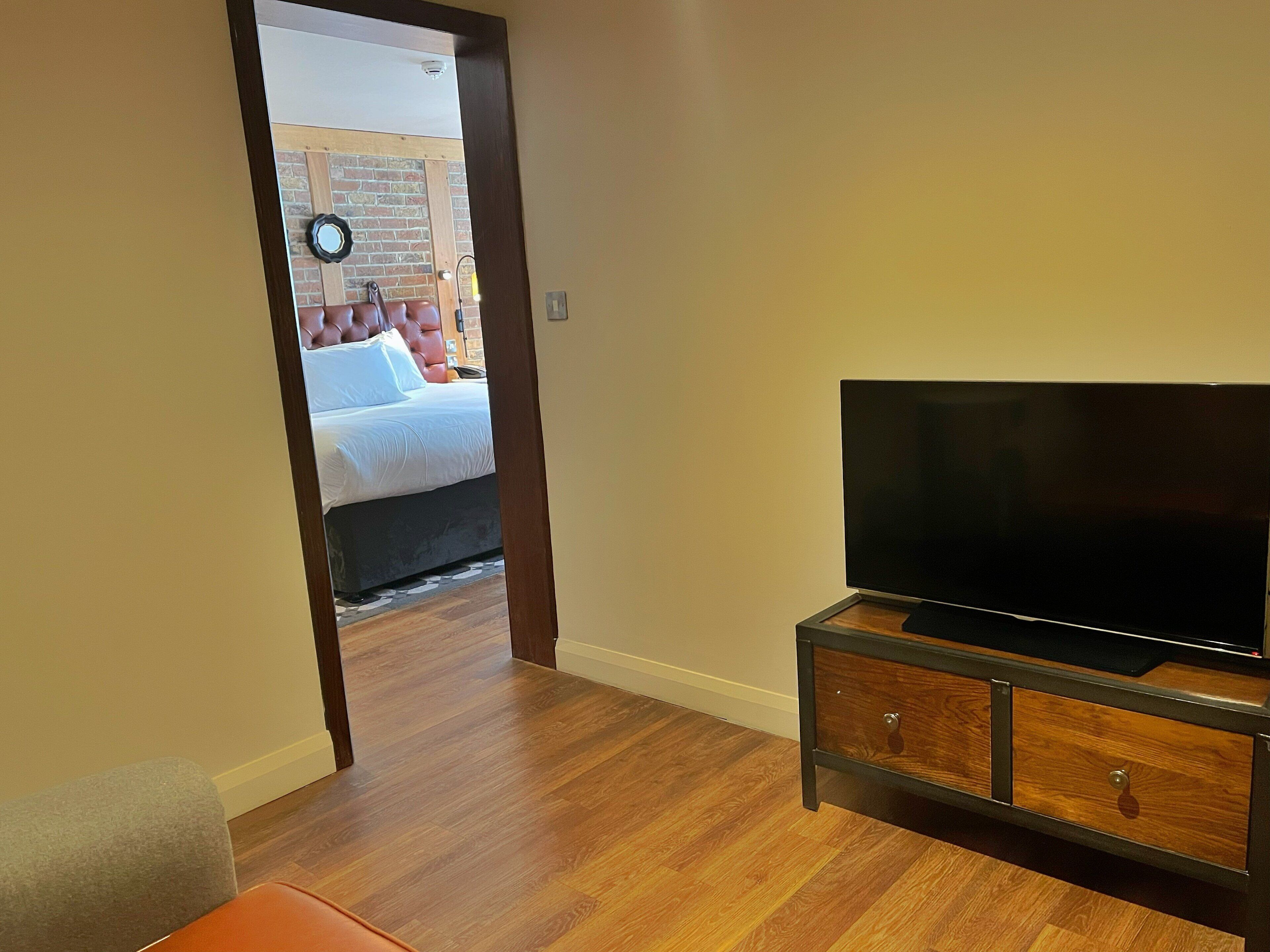 A room with a bed, a TV on a wooden cabinet, and a door leading to a balcony.