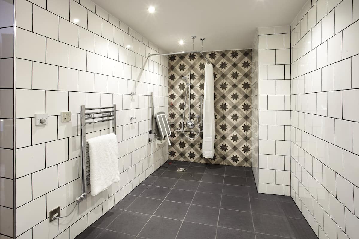 A bathroom with white and patterned tiles, a shower with a star pattern, and a towel rack with a white towel.