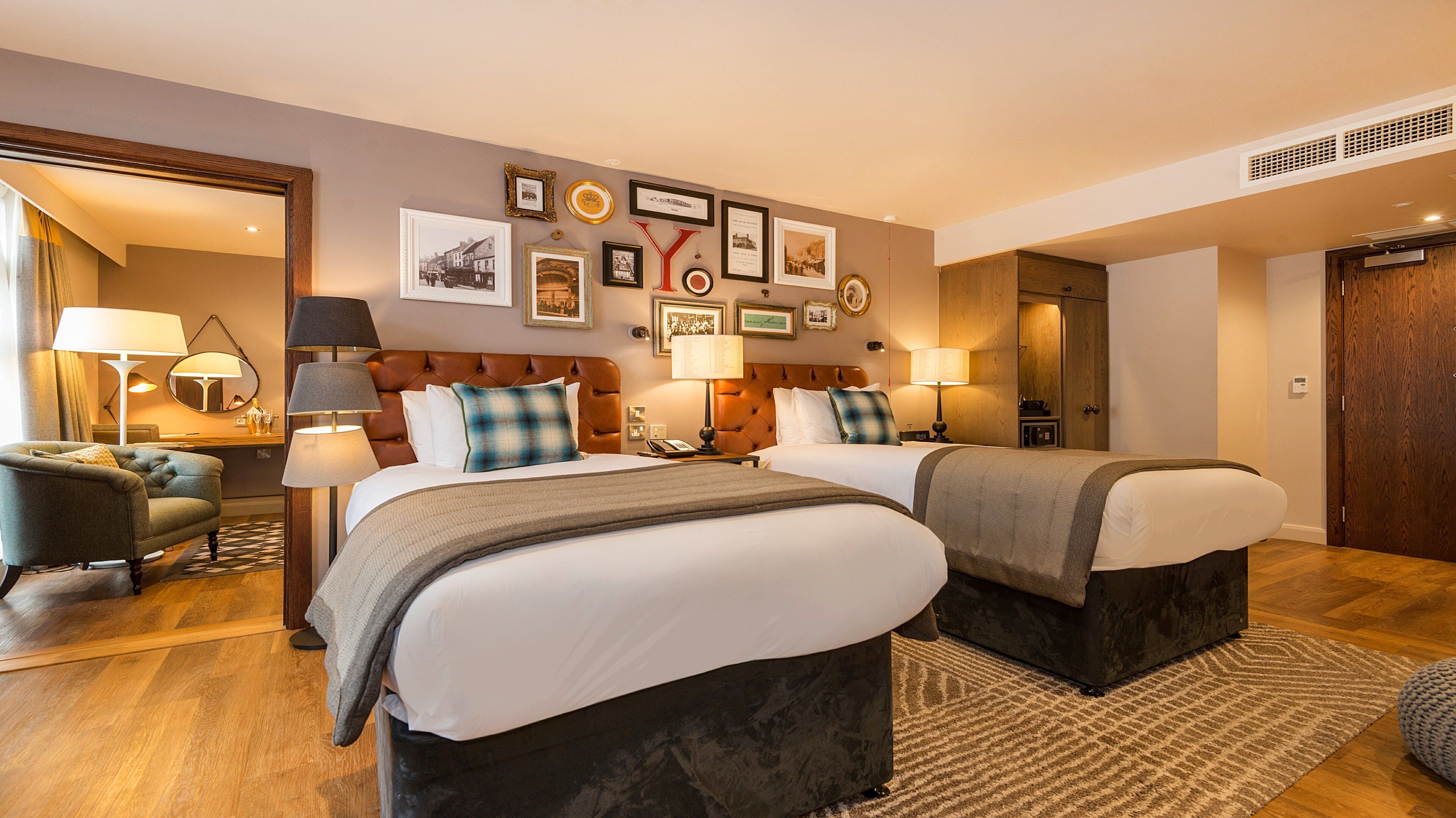 Une chambre d’hôtel avec deux lits, un coin salon avec un fauteuil, un bureau et une lampe.