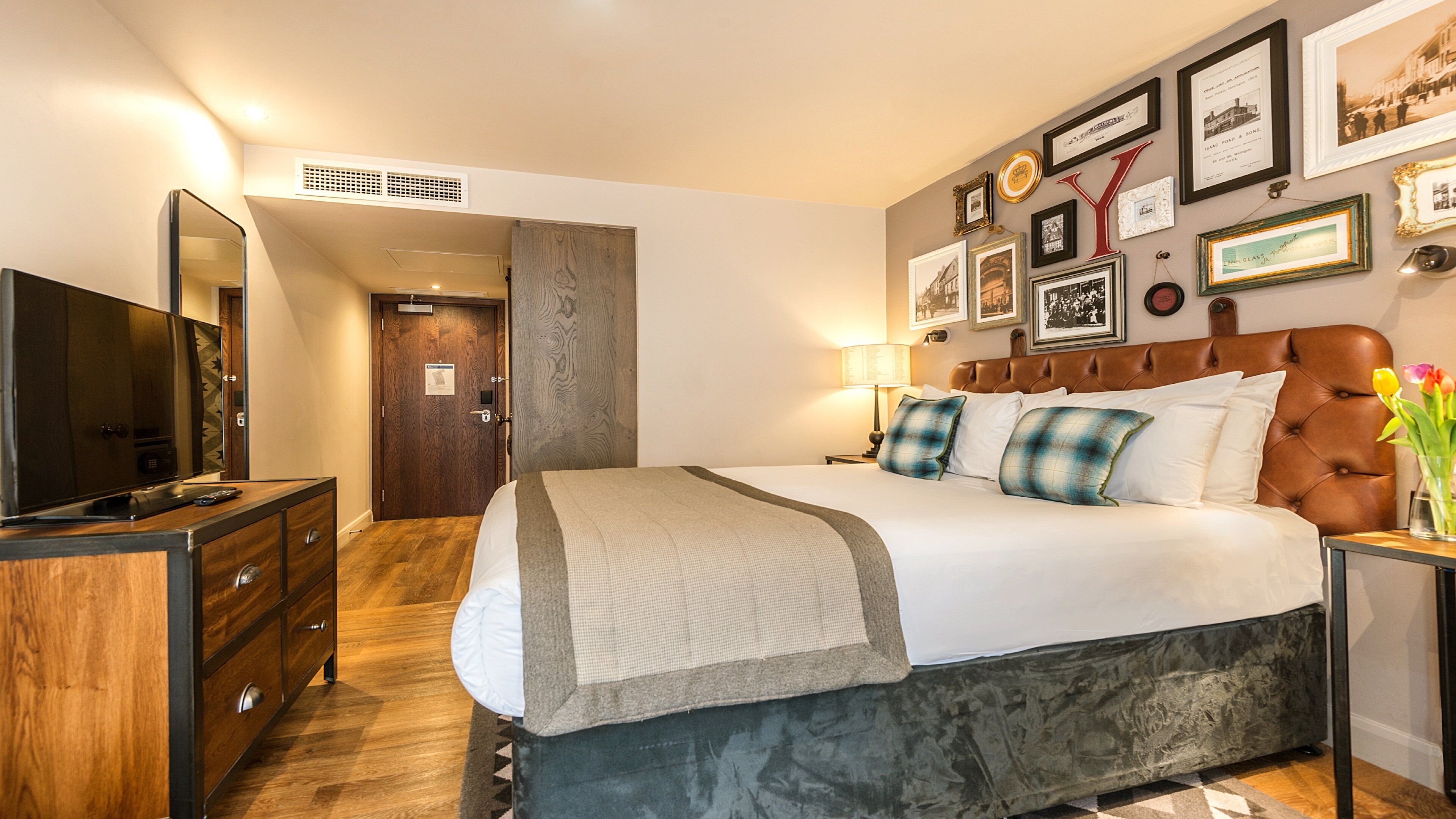 A bedroom with a bed, a television, a dresser, and a wall with framed pictures.
