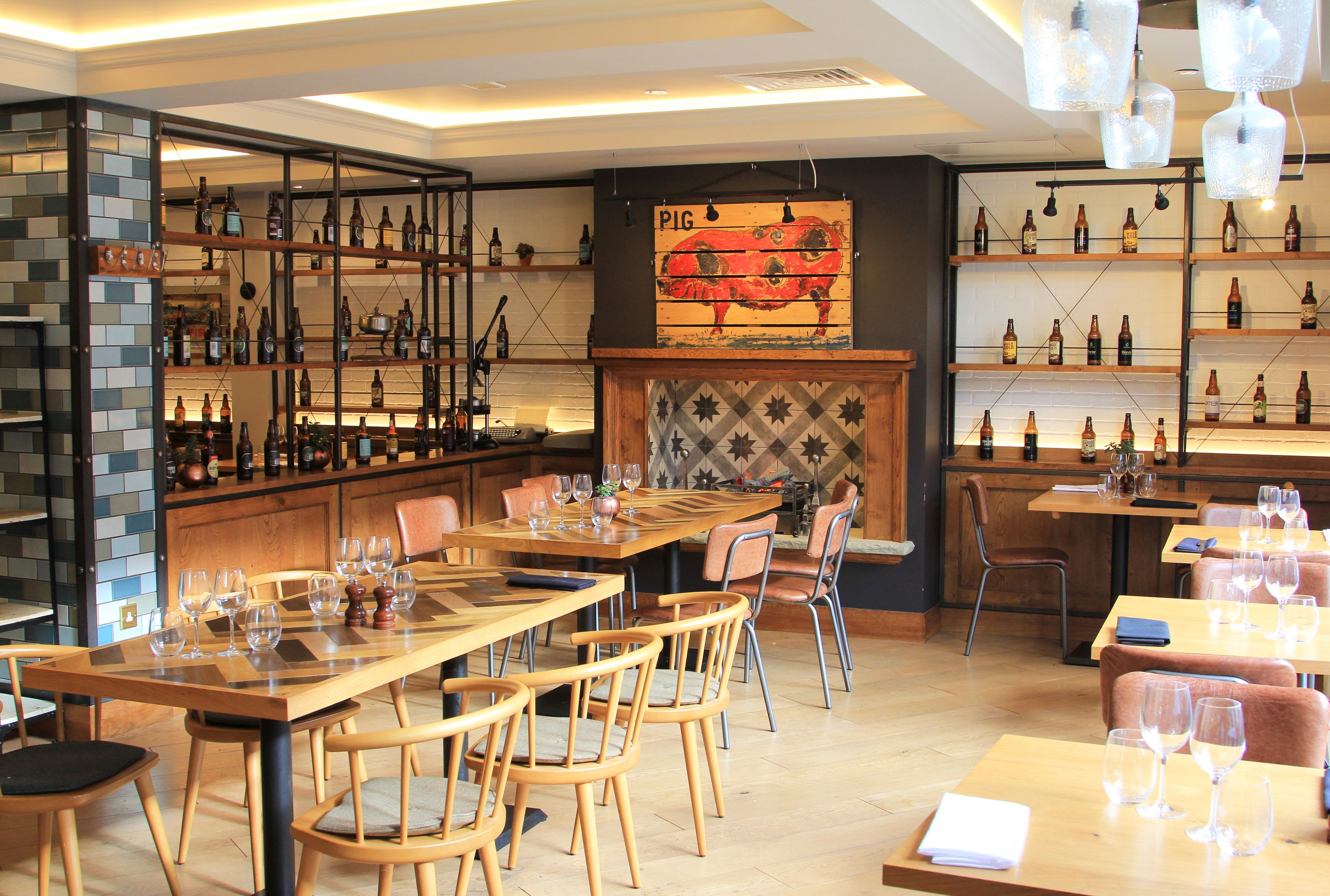 Un restaurante con mesas y sillas de madera, estanterías con botellas y una decoración de pared con motivos de cerdo.