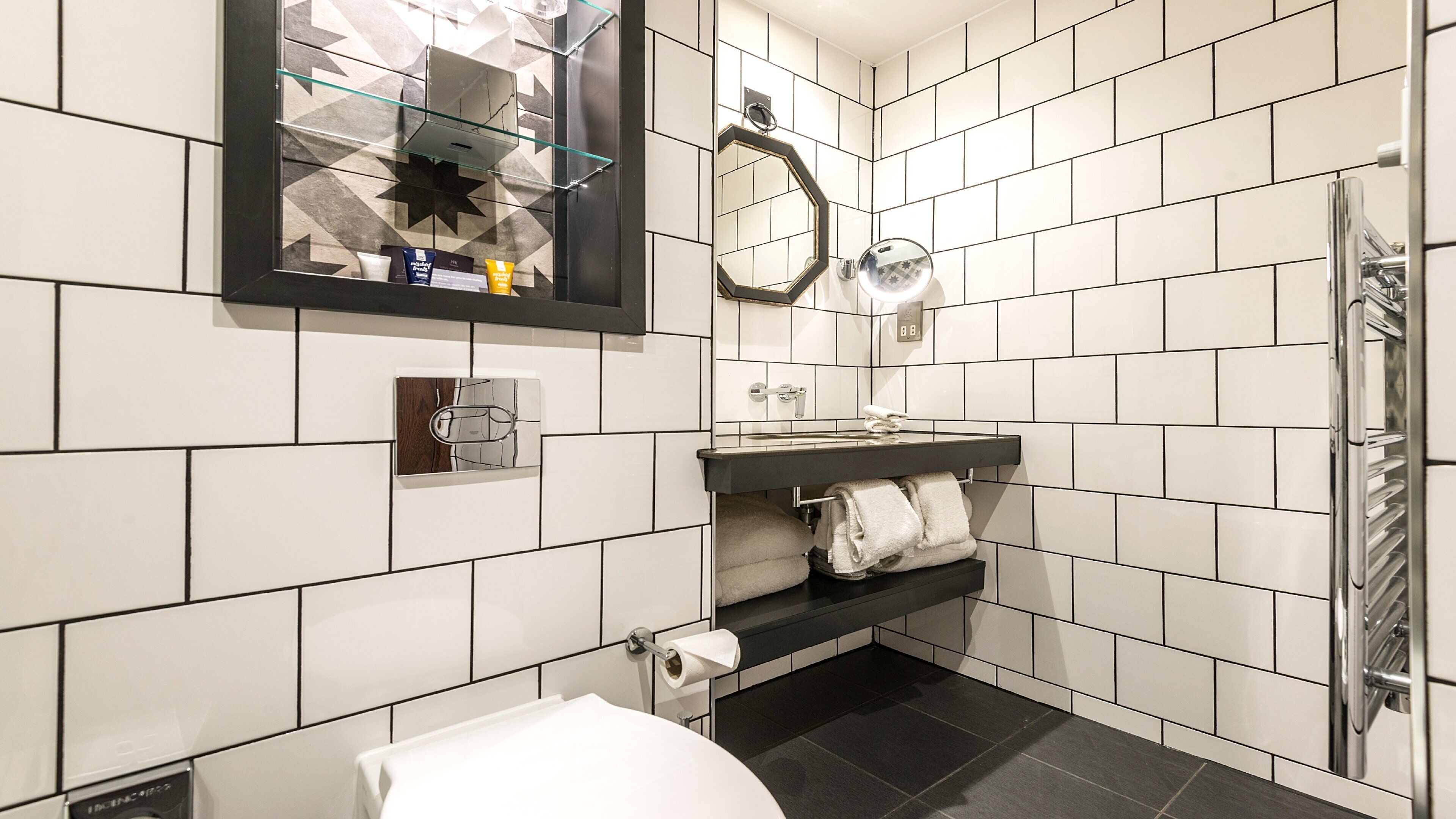 Un baño moderno con azulejos blancos, un lavamanos negro, cabina de ducha de vidrio y un espejo sobre el lavamanos.