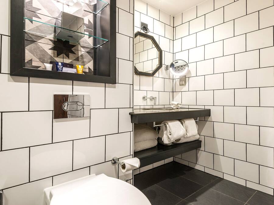 Un baño moderno con azulejos blancos, un lavamanos negro, cabina de ducha de vidrio y un espejo sobre el lavamanos.