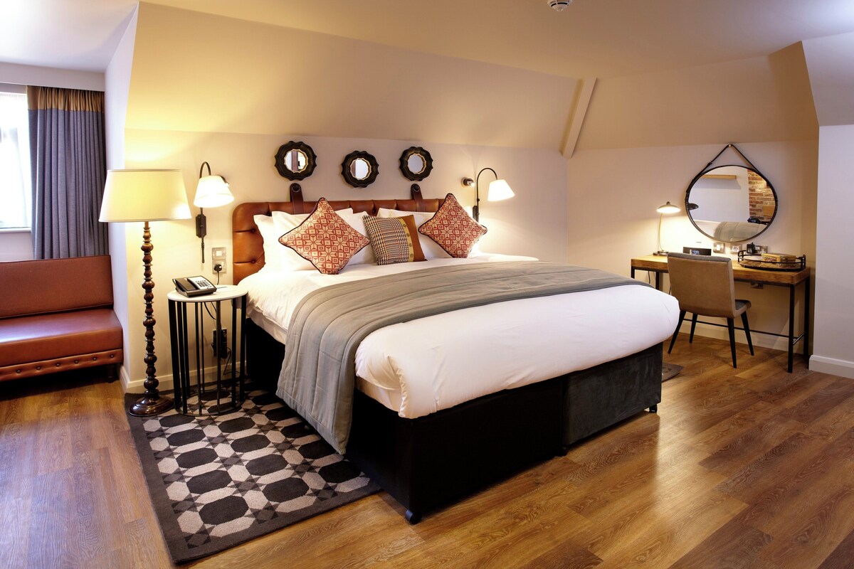 A bedroom with a bed, bedside lamps, a desk, a chair, a sofa, and a patterned rug.