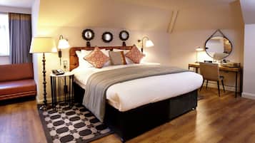 A bedroom with a bed, bedside lamps, a desk, a chair, a sofa, and a patterned rug.