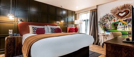 A hotel room with a large bed, dark wooden paneling, a red upholstered headboard, and a wall art piece with a heart design.