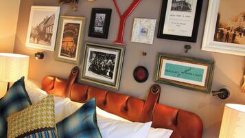 Une chambre à coucher avec une tête de lit en cuir, plusieurs tableaux encadrés accrochés au mur et une variété d’oreillers.