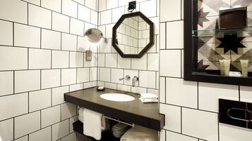 Un bagno moderno con parete rivestita in piastrelle bianche, lavabo con piano nero, specchio tondo e box doccia in vetro con motivo a stelle.