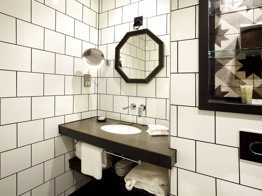 Un bagno moderno con parete rivestita in piastrelle bianche, lavabo con piano nero, specchio tondo e box doccia in vetro con motivo a stelle.