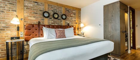 Un dormitorio con pared de ladrillo, cabecero capitonado, cama grande, dos mesitas de noche y un armario.