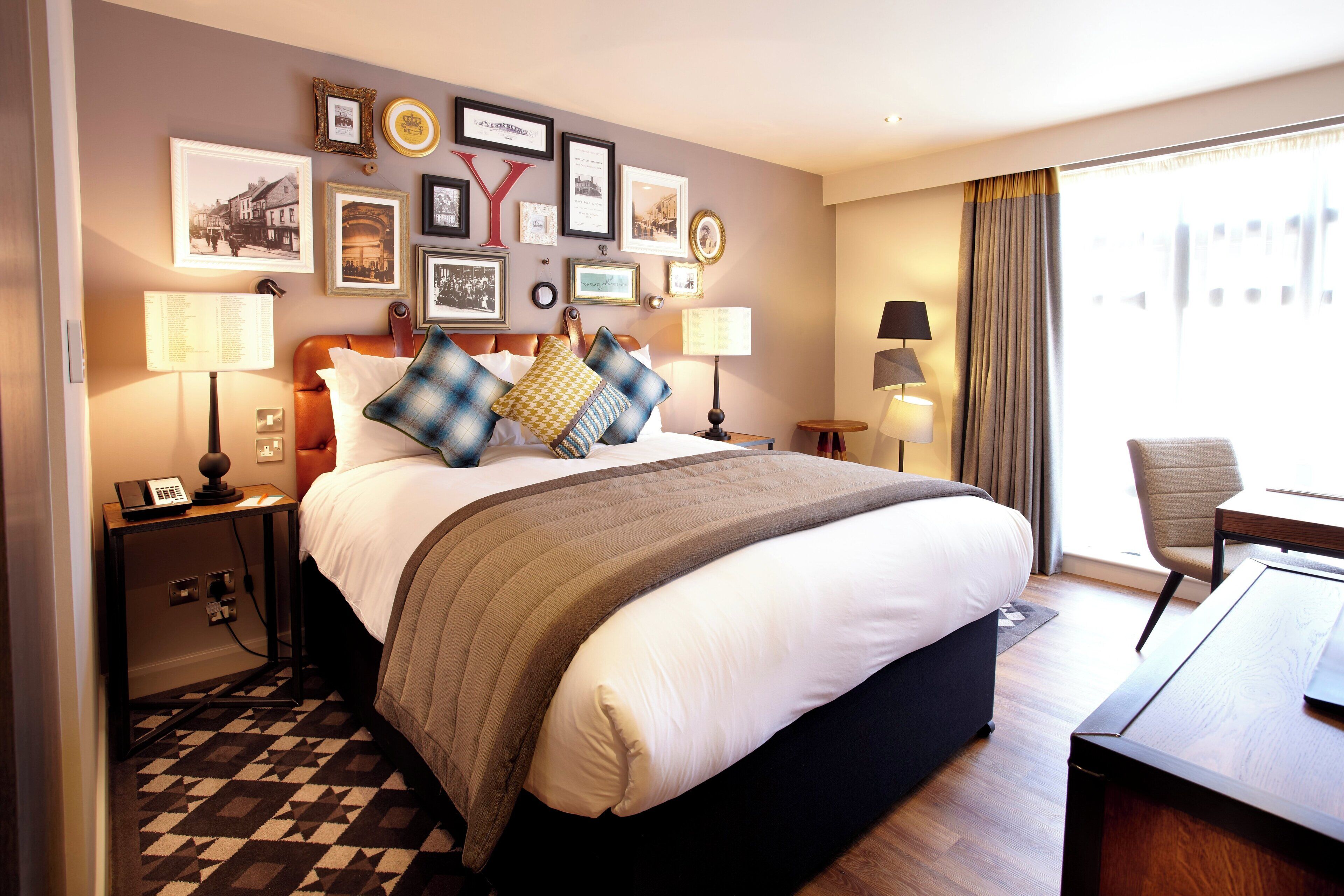 A hotel room with a large bed, two bedside tables with lamps, a desk with a chair, and a view of the city through the window.
