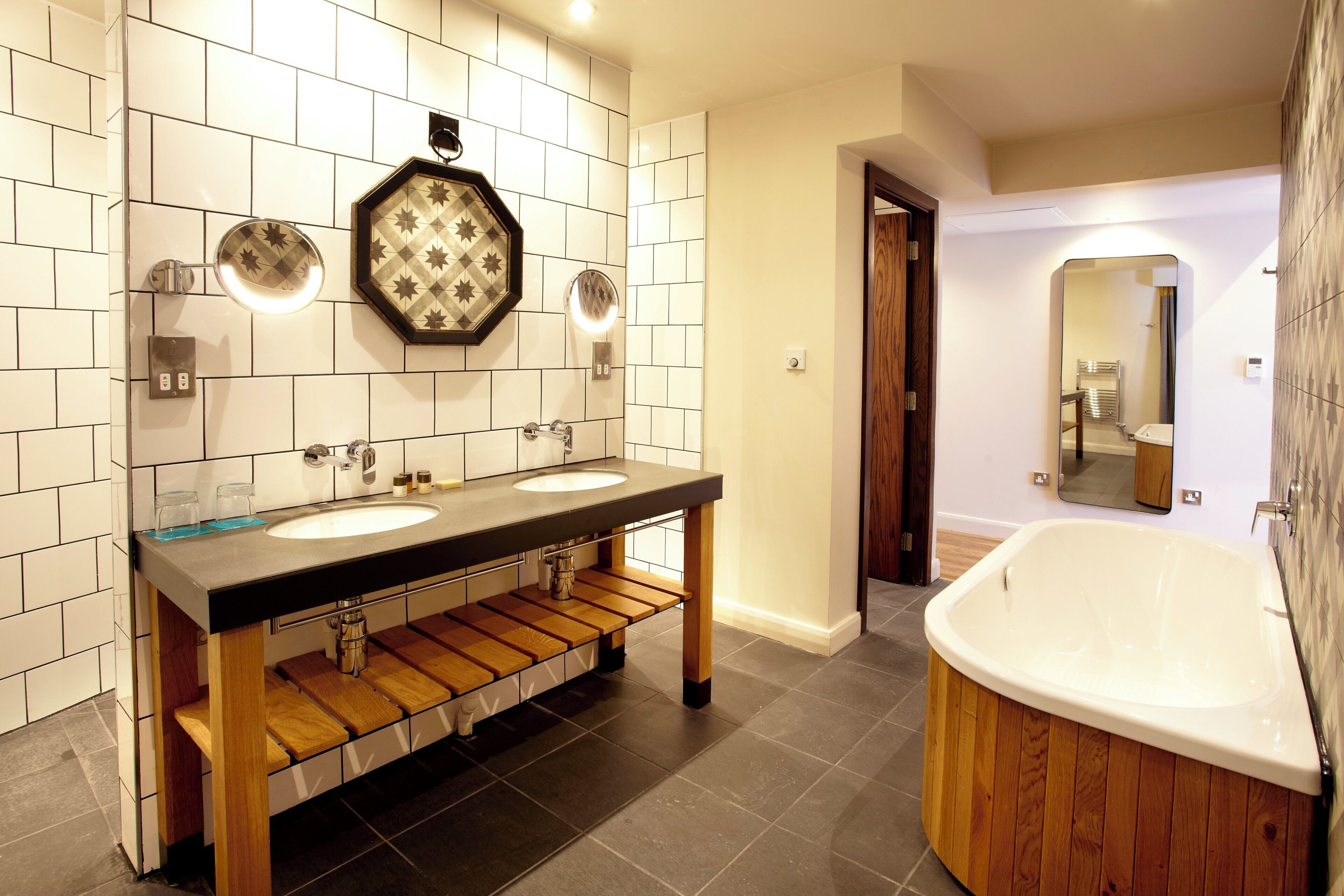 A modern bathroom with a wooden vanity, two sinks, a large bathtub, and a mirror.