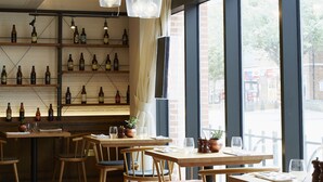 Ein Restaurantinnenraum mit Holztischen und -stühlen, hängenden Pendelleuchten und Regalen mit Flaschen.