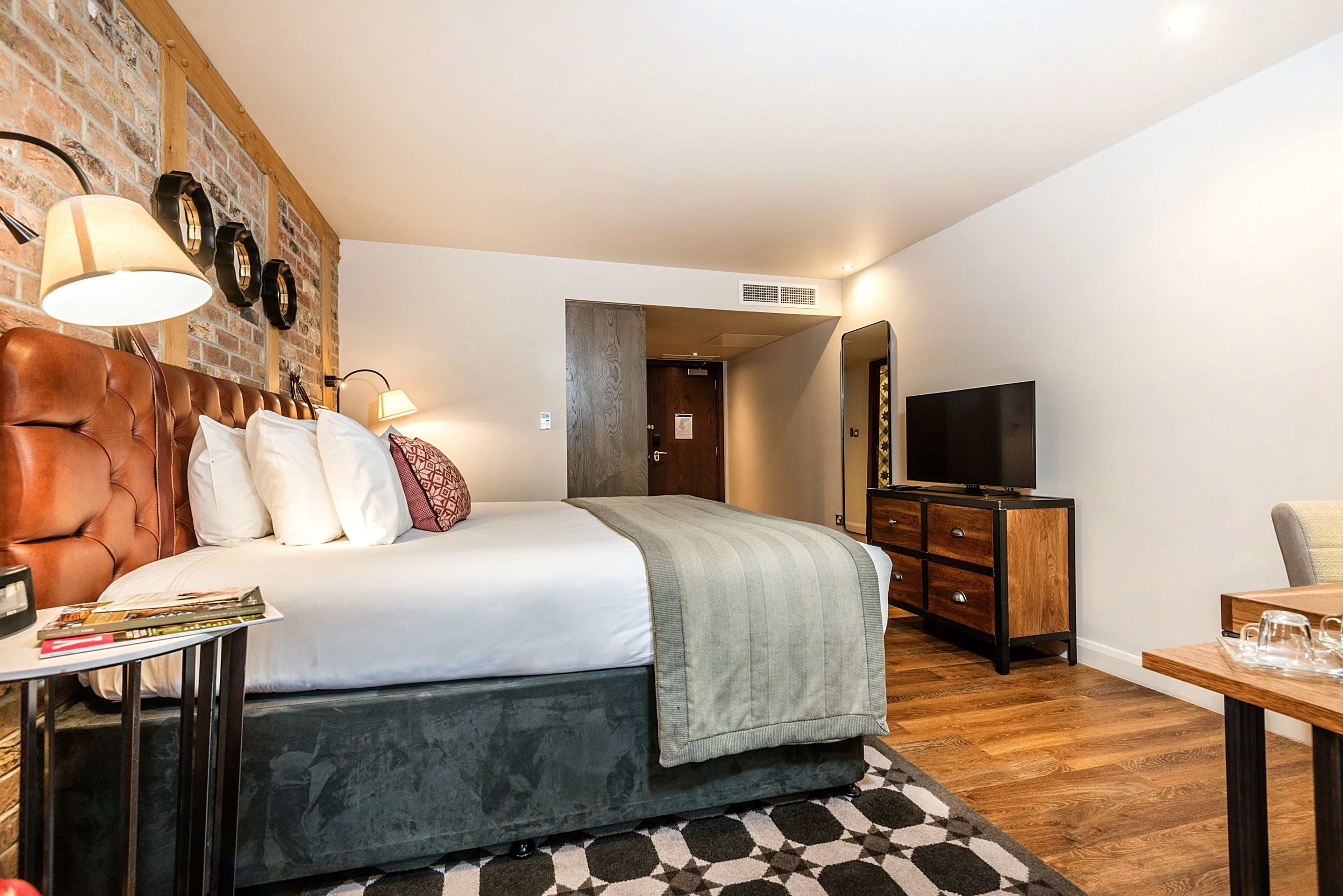 Een slaapkamer met een bed, nachtkastje, lamp en een televisie.