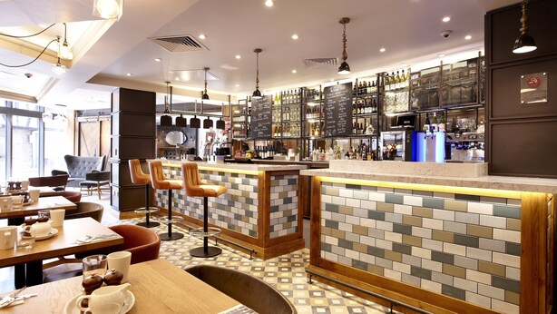 Eine moderne Bar mit einer gefliesten Rückwand, Barhocker und einer Auswahl an Flaschen und Gläsern auf Regalen.