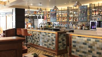 Zona de bar con salpicadero de azulejos, mostrador de madera y diversas botellas y vasos en estantes.