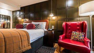 A hotel room with a large bed, a red armchair, and a wooden nightstand.
