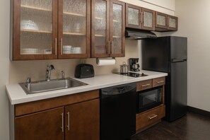 A kitchen with wooden cabinets, a dishwasher, a refrigerator, and a coffee maker. - Candlewood Suites Vancouver-Camas by IHG (Vancouver)