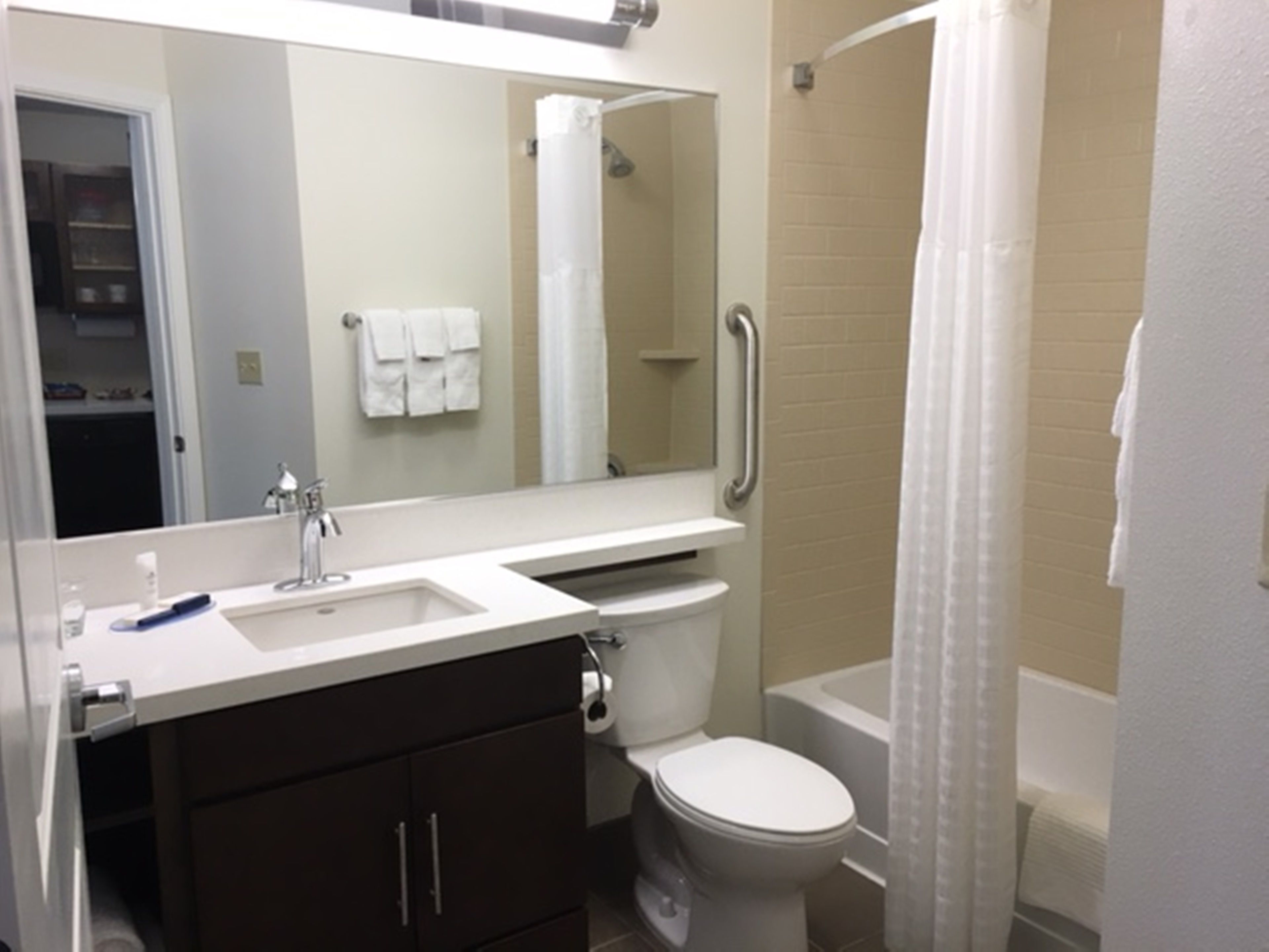 Un bagno con lavandino bianco, specchio e water. Si intravede una tenda da doccia e una vasca da bagno.