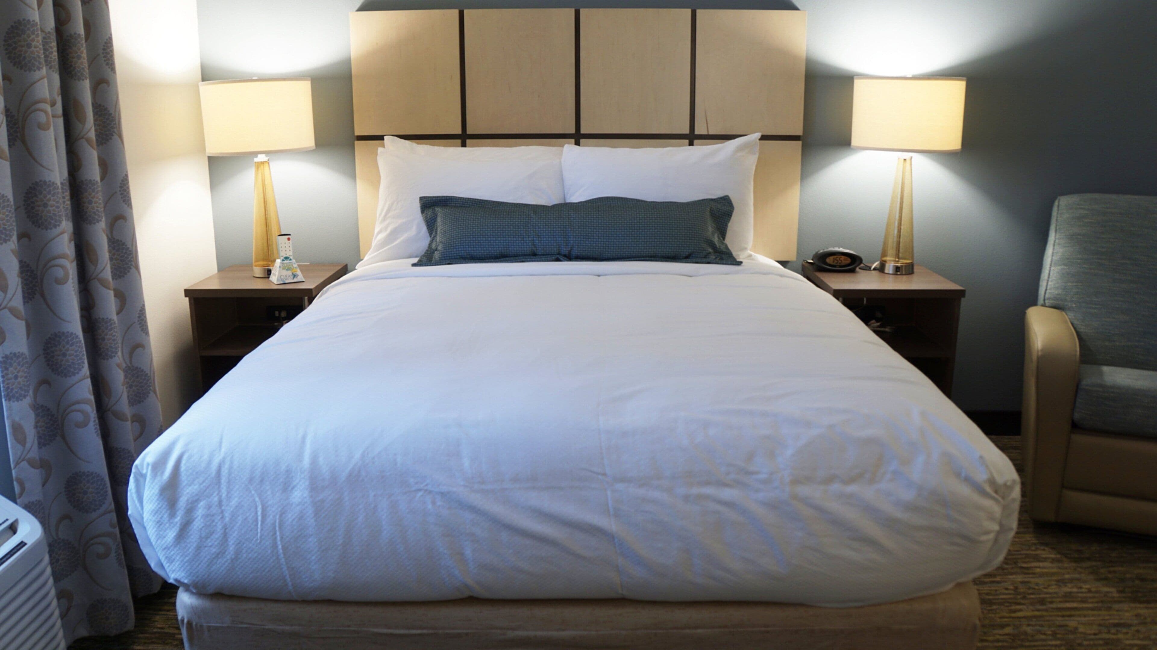 A hotel room with a large bed, two bedside tables with lamps, a chair, and a curtain.