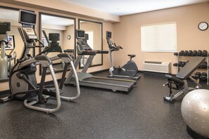 Une salle de sport équipée de tapis de course, de vélos elliptiques, d’un rameur et de poids libres.