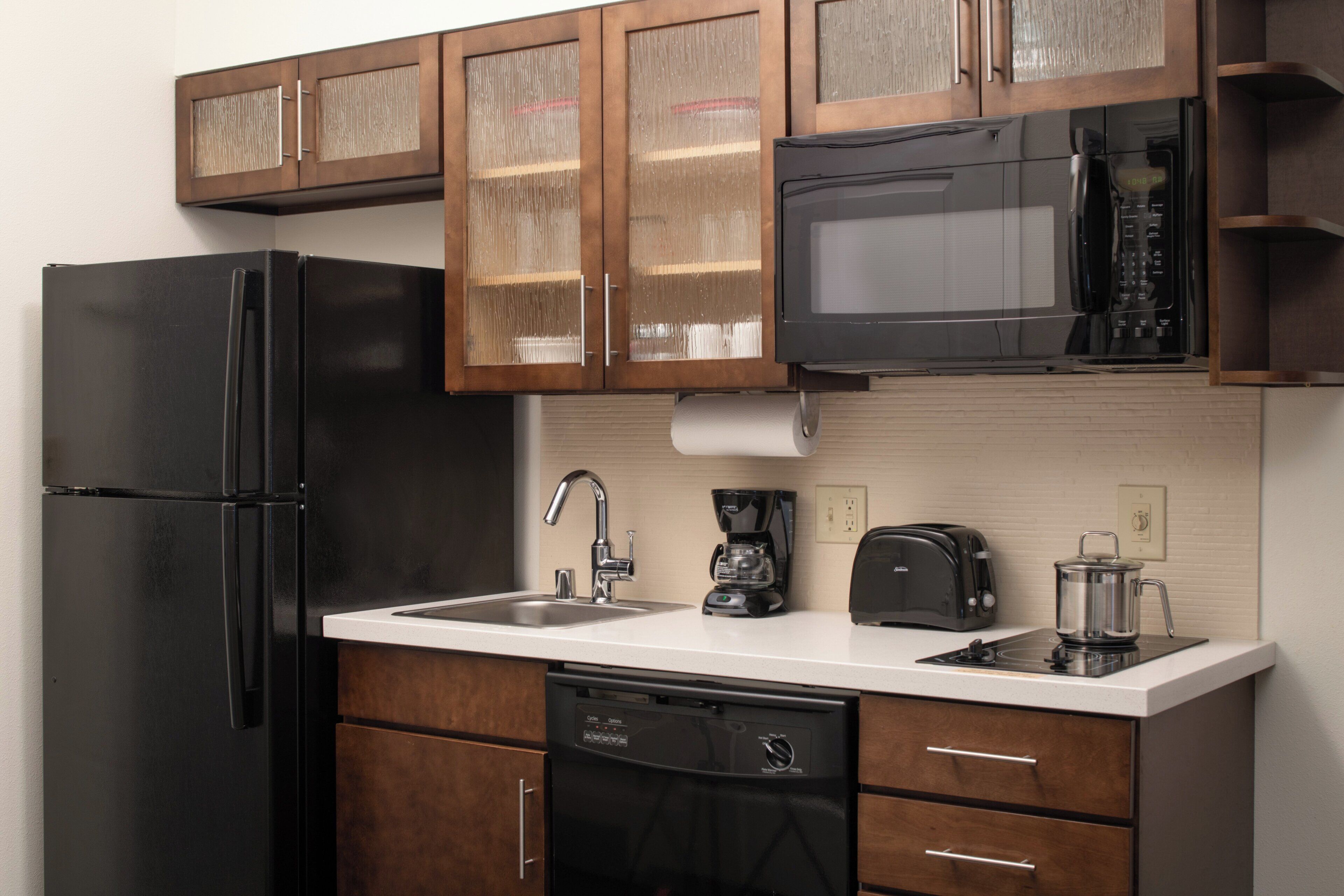 Una cocina con un refrigerador negro, un microondas, una cafetera y un tostador.