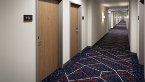 Un pasillo de hotel con puertas de madera, letreros de habitaciones numeradas y una alfombra estampada.