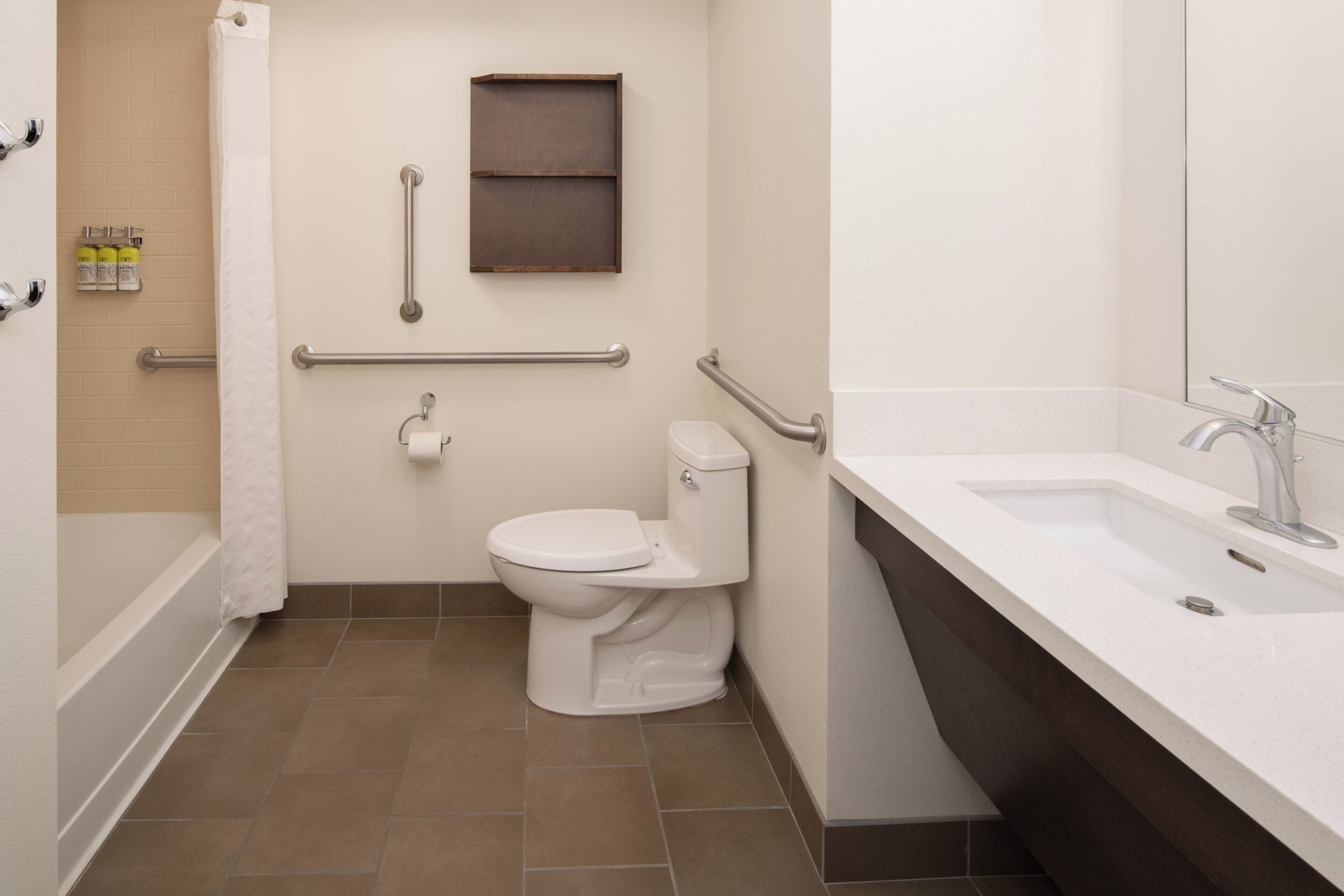 Un baño con inodoro blanco, lavabo y bañera. Cuenta con barras de apoyo para mayor seguridad.