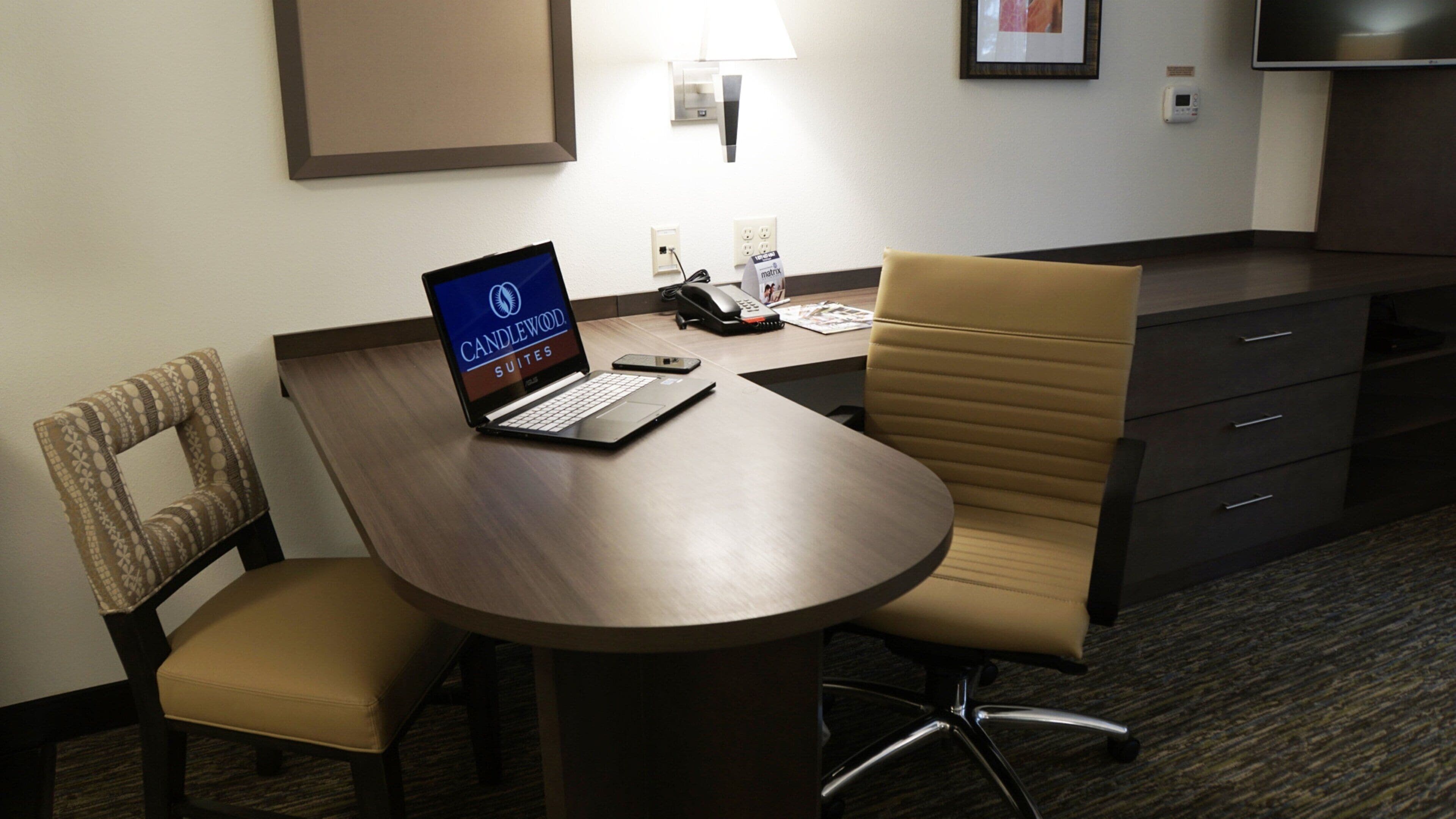 A hotel room with a desk, laptop, telephone, and a chair.