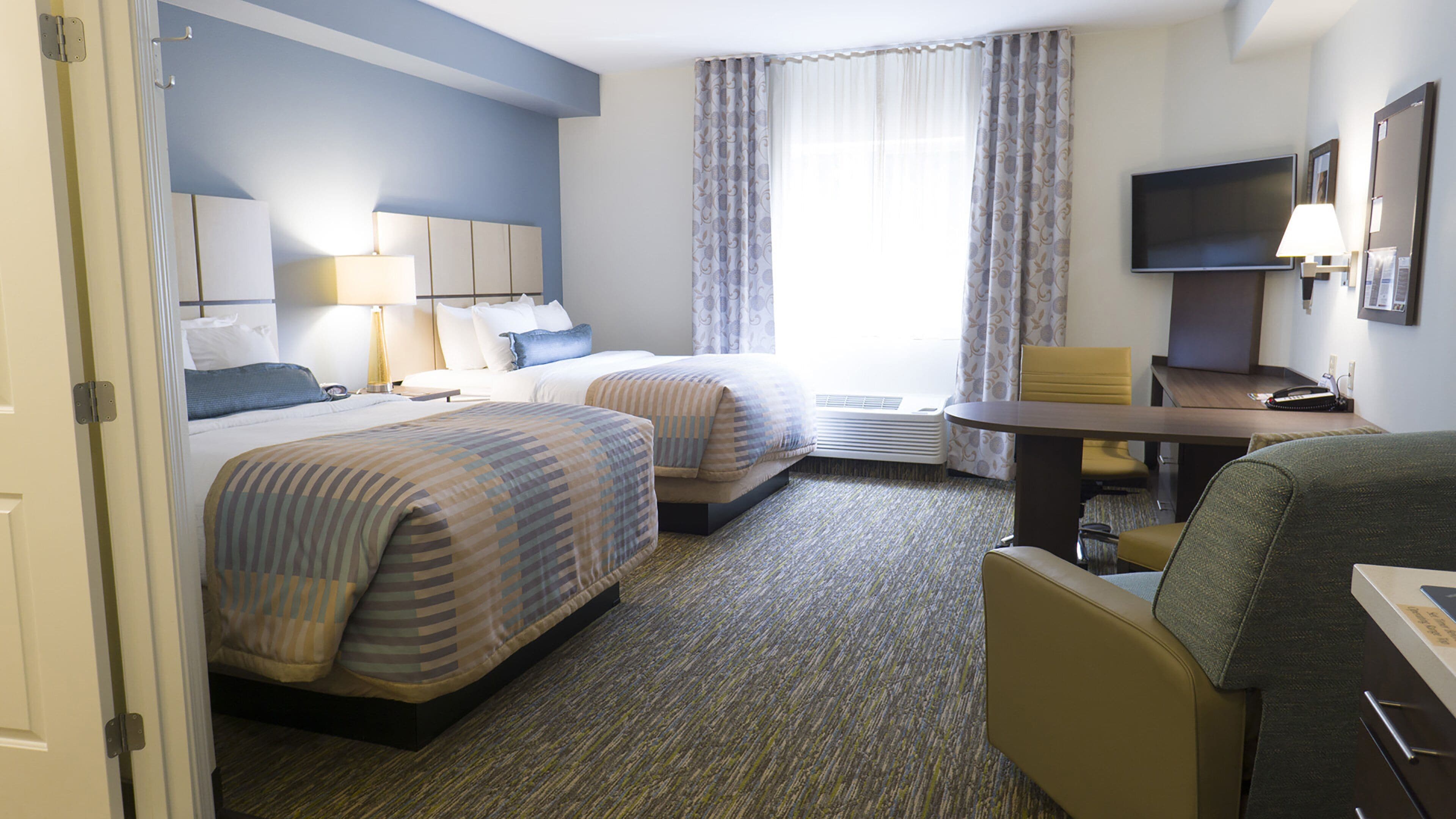 A hotel room with two beds, a desk, a chair, a TV, and a window with curtains.