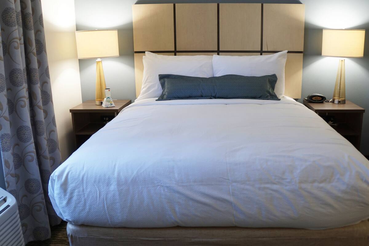 Una habitación de hotel con una cama grande, dos mesitas de noche con lámparas, una silla y una cortina.