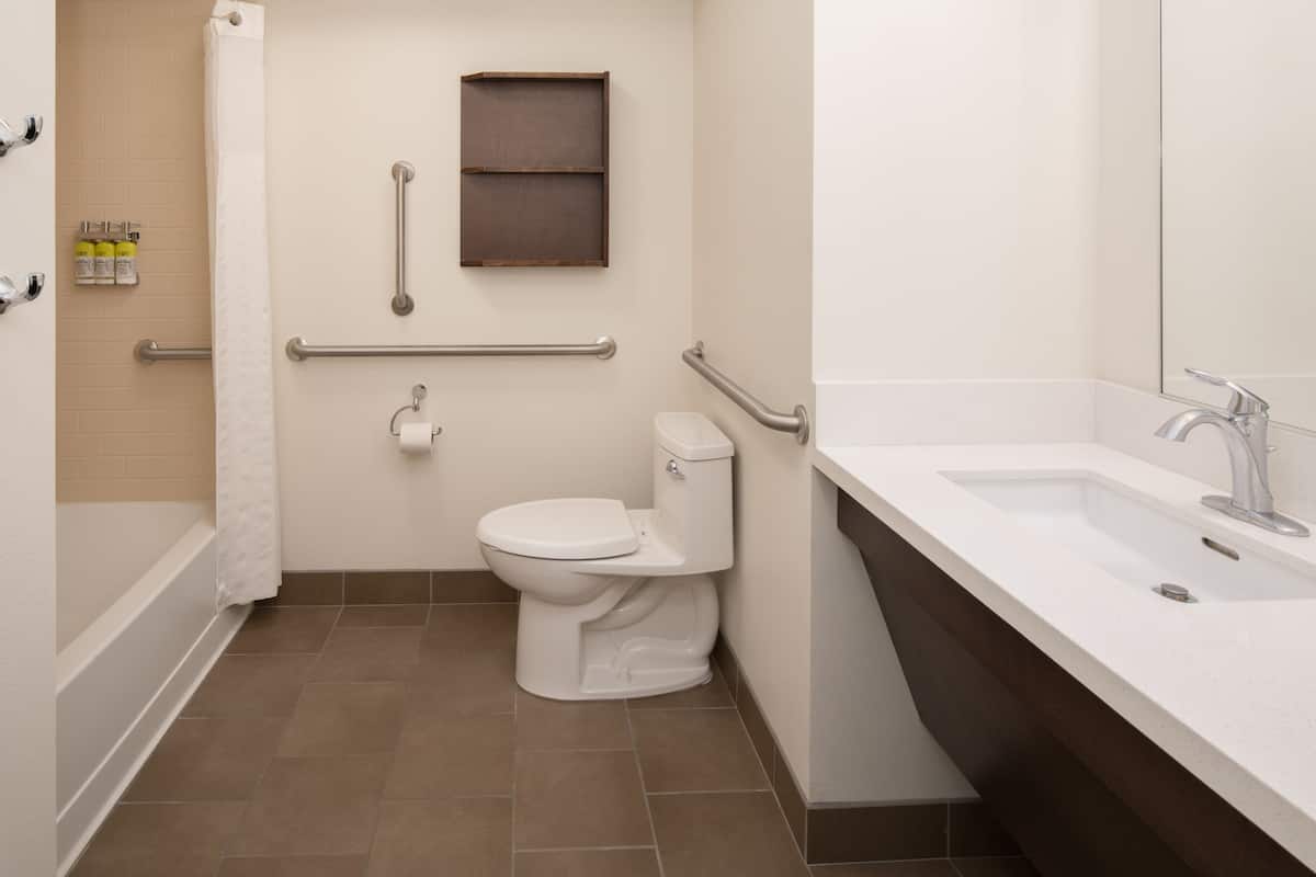 Un baño con inodoro, barras de apoyo, ducha y lavamanos.