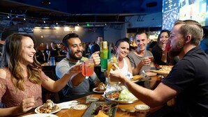 Un grupo de personas brindando con bebidas en un bar con varios platos sobre la mesa.