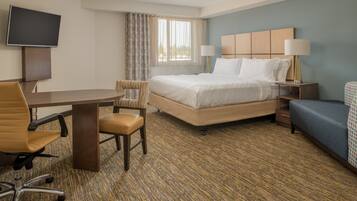 A hotel room with a bed, a desk, a chair, a TV, and a lamp.